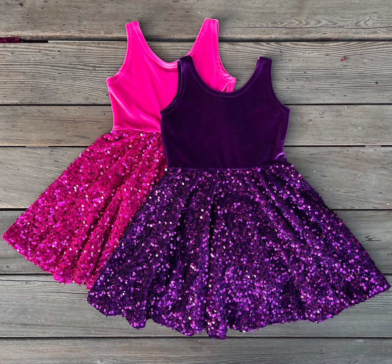 Two sparkly dresses, one pink and one purple, on a wooden surface.