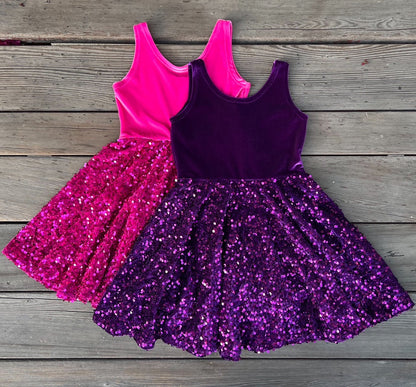 Two sparkly dresses, one pink and one purple, on a wooden surface.
