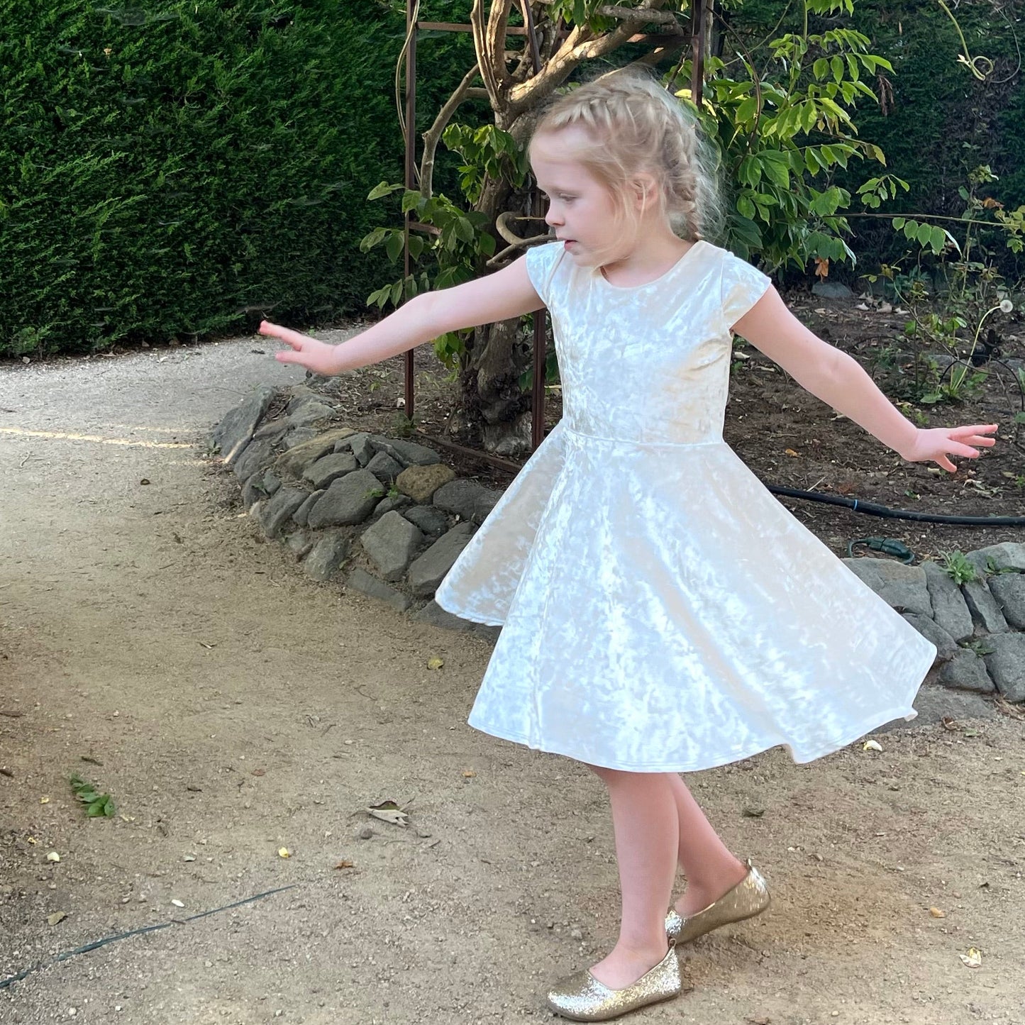 Young girl in a white dress standing outdoors on a path with greenery in the background